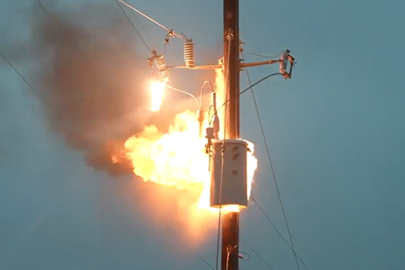 Pole-mounted distribution transformer emitting smoke and sparks during a failure event